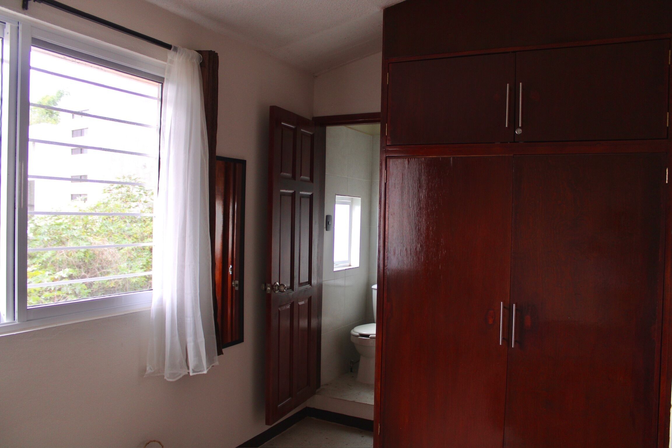 A bathroom with a toilet, a mirror, and a window with curtains.