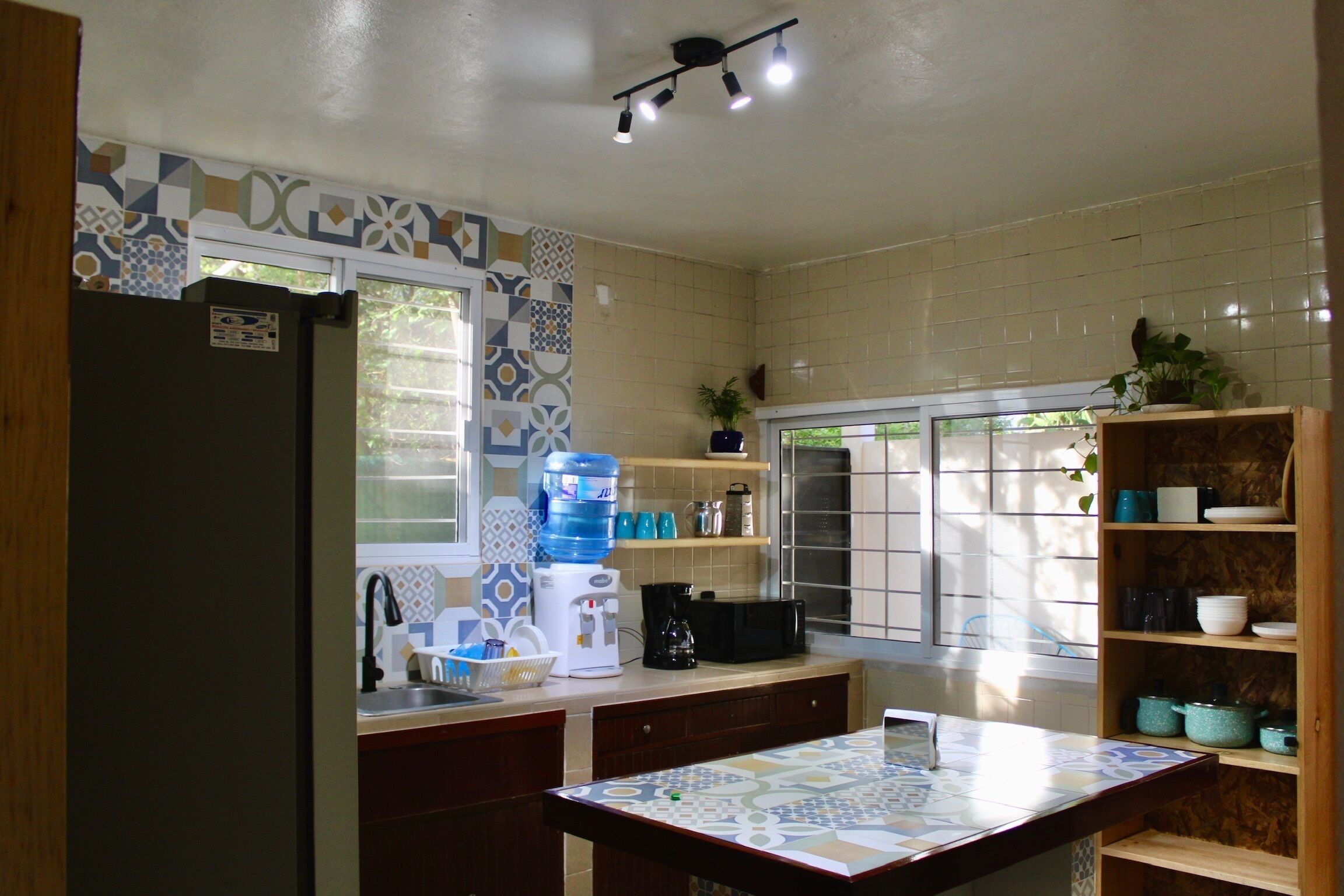 Una cocina con refrigerador, lavaplatos, mostrador y repisas con utensilios de cocina.