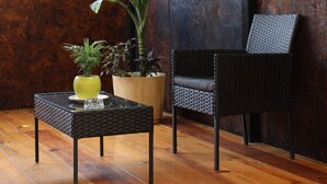 A room with a wooden floor, a table with a vase and a plant, a chair, and a wall with a textured surface. - Luffa Hostel (Oaxaca)