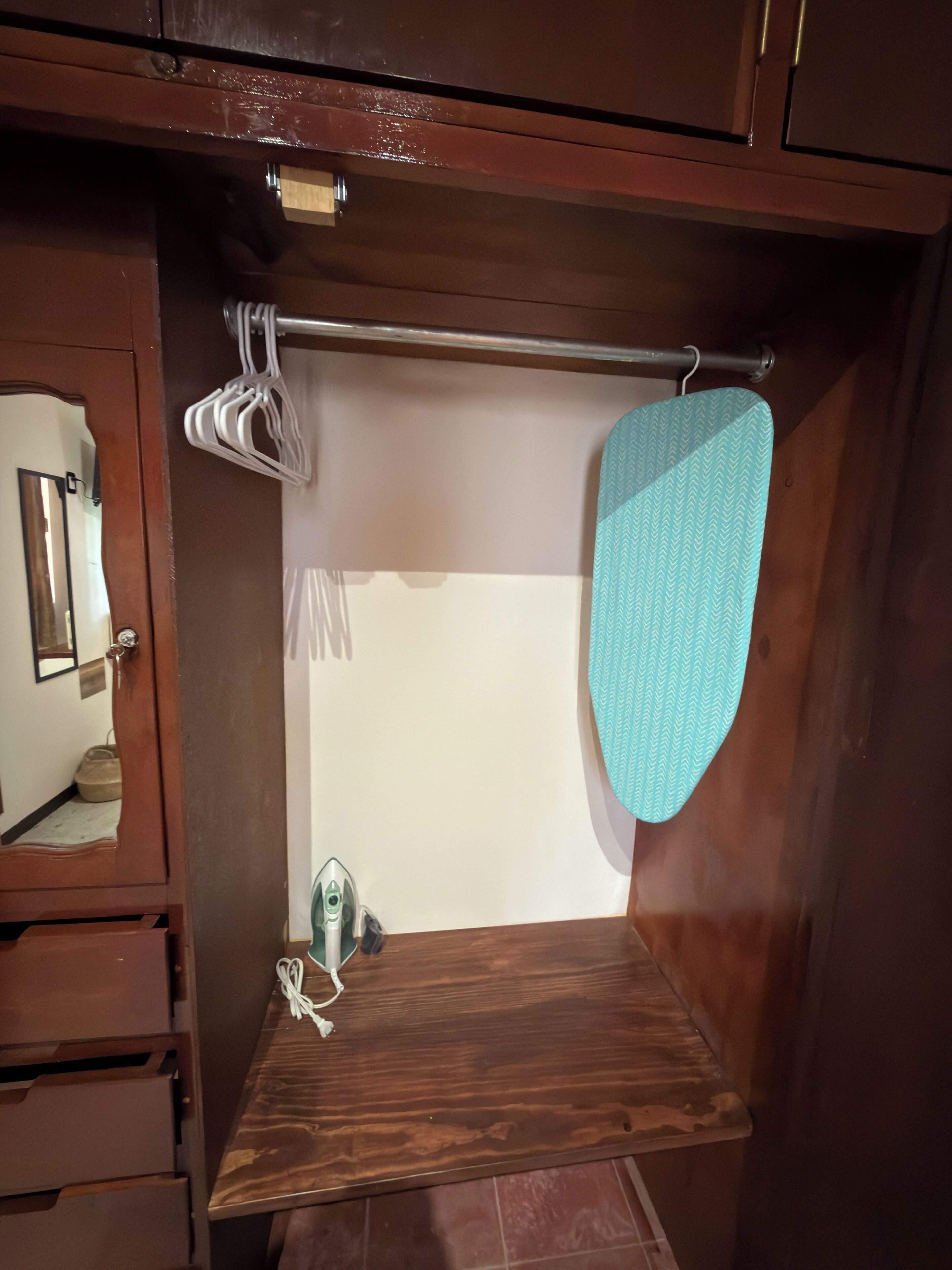 Een houten kast met spiegel, een kledingrek en een klein strijkplank.