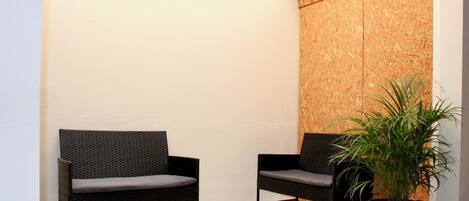 A corner with two wicker chairs, a potted plant, and a wooden wall.