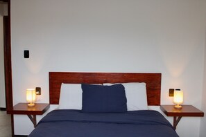 A bed with a wooden headboard, two bedside tables with lamps, and a white wall.