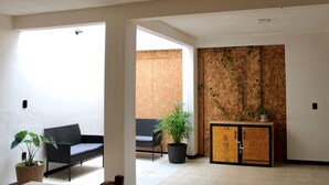 An interior space with a sofa, a potted plant, a cabinet, and a wall with a wooden panel design. - Luffa Hostel (Oaxaca)