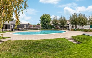 Ein Schwimmbecken mit Pflasterung aus Ziegelsteinen, umgeben von Gras und Bäumen.
