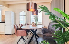 Een eetgedeelte met een ronde tafel, stoelen, een hanglamp, een vaas met bloemen en een bank.