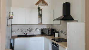 Ett modernt kök med vita skåp, en mikrovågsugn, en spis och en hängande lampa.
