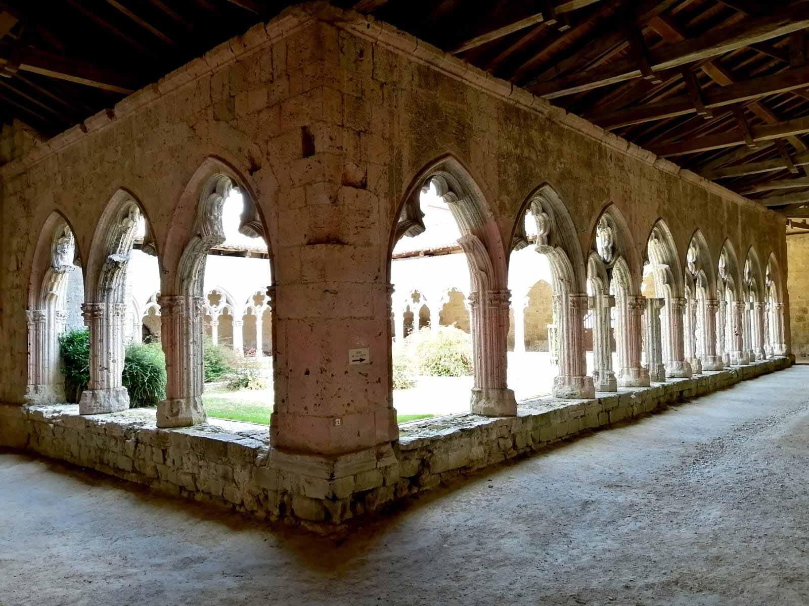 Interno caratterizzato da una serie di archi e colonne, un pavimento in pietra e vista sul verde circostante.