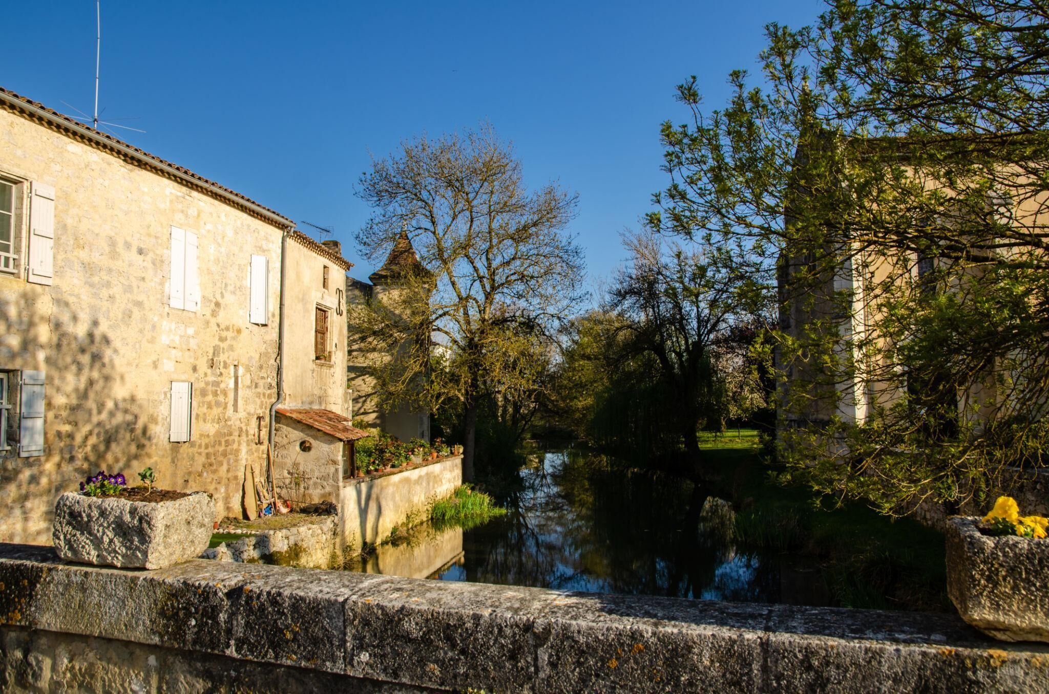 A stone building with a window and a door, a narrow waterway, and trees.