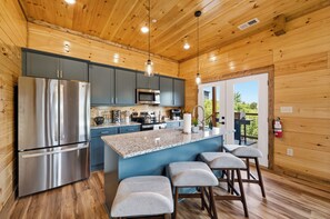 A modern kitchen with a stainless steel refrigerator, a microwave, and a granite countertop island with bar stools. - New! Our Get-Together Place! Indoor Heated Pool, Views, Games, Hottub, Theatre! (Sevierville)