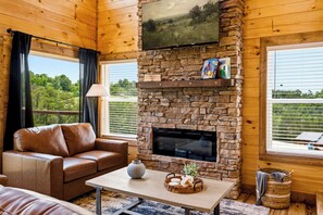 A cozy room with a stone fireplace, leather sofa, and a flat-screen TV mounted above it. - New! Our Get-Together Place! Indoor Heated Pool, Views, Games, Hottub, Theatre! (Sevierville)