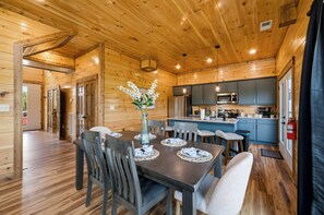 A wooden cabin interior with a dining area, kitchen, and a small living space. - New! Our Get-Together Place! Indoor Heated Pool, Views, Games, Hottub, Theatre! (Sevierville)