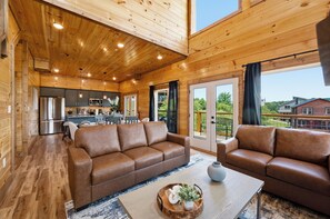 A wooden cabin interior with a living area, kitchen, and large windows. - New! Our Get-Together Place! Indoor Heated Pool, Views, Games, Hottub, Theatre! (Sevierville)