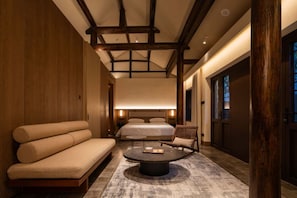 Habitación de hotel moderna con una cama grande, un sofá, una mesa redonda de centro y vigas de madera en el techo.
