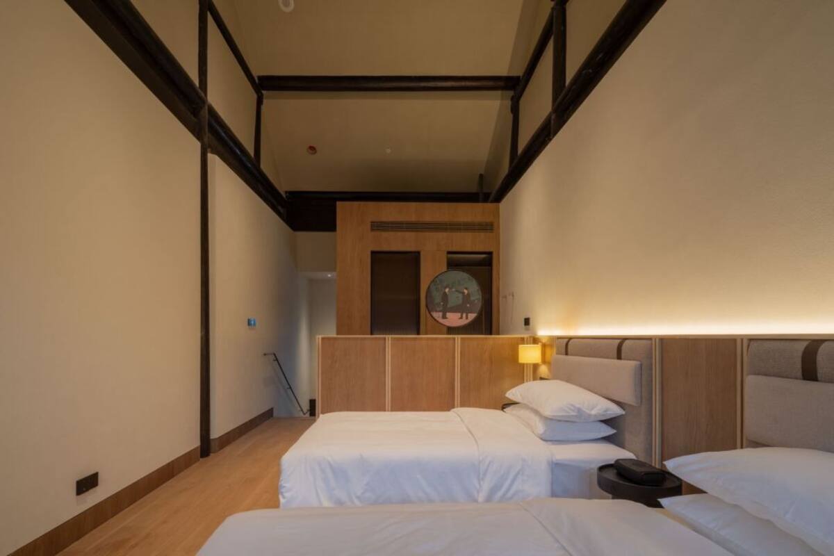 A hotel room with two beds, a wooden headboard, a wall-mounted picture, and a lamp.