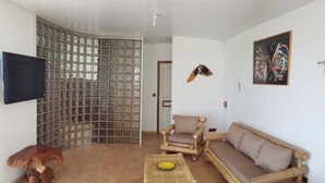 A living room with a sofa, armchairs, a coffee table, a TV, and a decorative wall piece. - MA Season, 2 detached four-bedroom villas for groups or families of 6 to 12 people (Sainte-Luce)