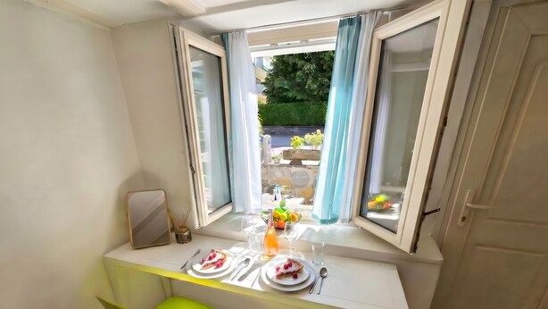A dining area with a table set for two, a window with curtains, and a view of the outdoors. - Casa Cecilia Ascona 500m from the Lake, Ascona, Switzerland (Ascona)