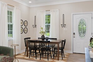 Un coin repas avec une table en bois, des chaises noires, des rideaux blancs et un vase rempli de fleurs.