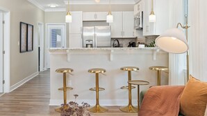 Una cocina moderna con gabinetes blancos, electrodomésticos de acero inoxidable y taburetes dorados.