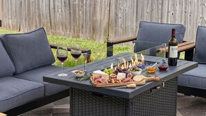 Un patio al aire libre con una mesa dispuesta para una comida, incluyendo queso, carnes, frutas y copas de vino.