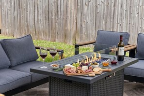 Eine Terrasse im Freien mit einem Tisch, der für eine Mahlzeit gedeckt ist, darunter Käse, Fleisch, Früchte und Weingläser.