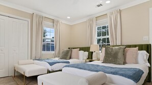 Habitación de hotel con dos camas, zona de estar, ventana con cortinas y puerta.