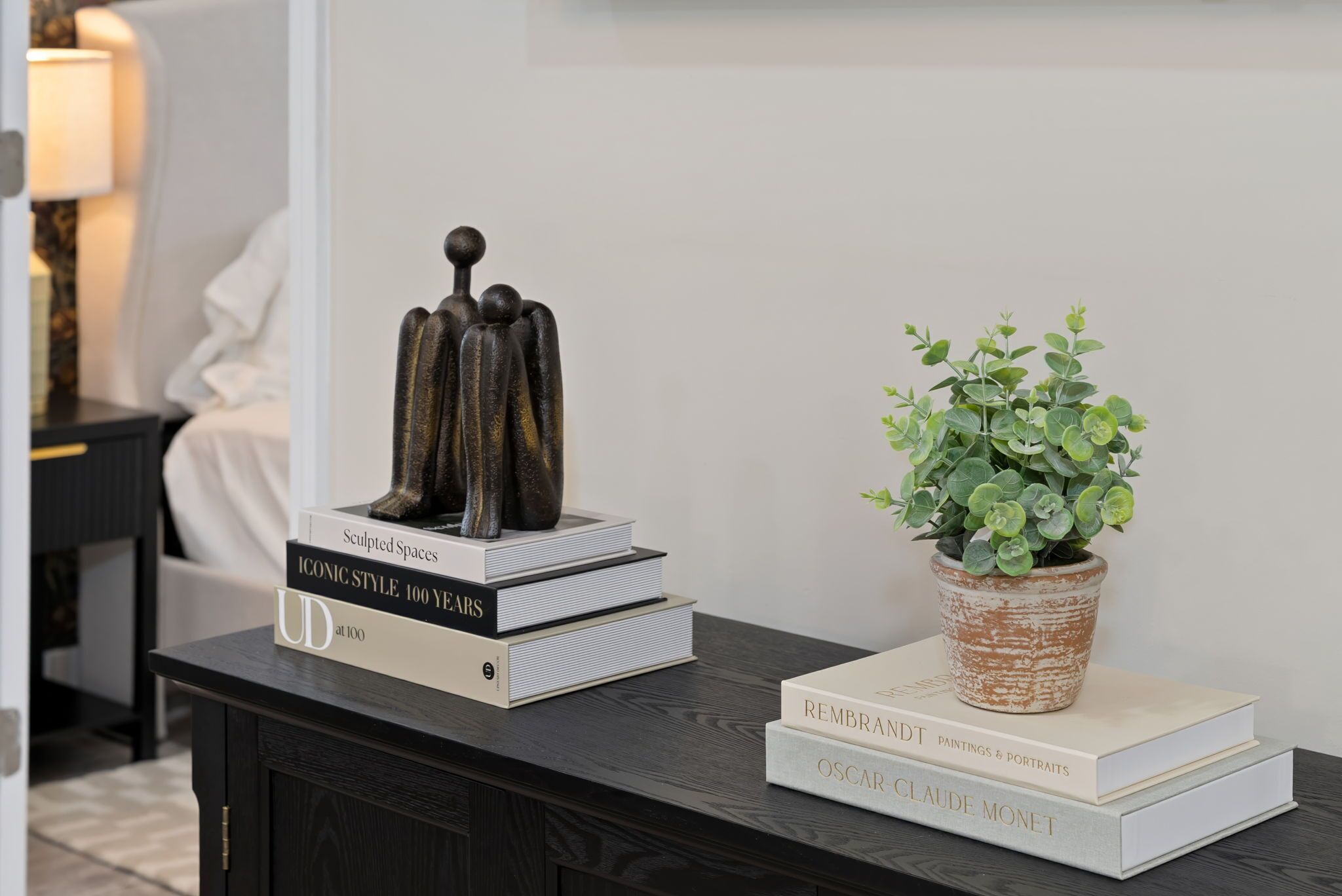 Une table en bois foncé, ornée d’une sculpture, de livres et d’une plante en pot.