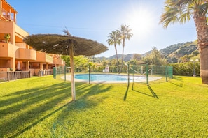 A swimming pool surrounded by a fence, a palm tree, and a building with balconies. - Reserva De Marbella 2 Sunviews, Marbella, Spain (Marbella)