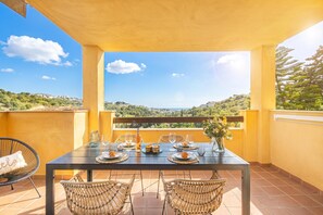 A balcony with a table set for dining, wicker chairs, and a view of the landscape. - Reserva De Marbella 2 Sunviews, Marbella, Spain (Marbella)