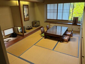 Ein Raum mit Tatami-Matten, einem Holztisch und -stühlen, einem Shoji-Bildschirm und Blick auf Grünfläche.
