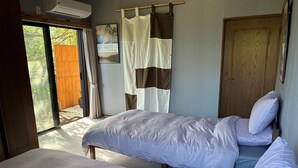 A bedroom with two beds, a wooden door, a window with curtains, and a wall-mounted air conditioner.