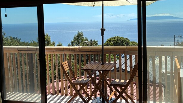 A balcony with a table and chairs, a view of the sea, and bamboo railings.