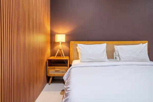 Cama bem arrumada com lençóis brancos, cabeceira de madeira e mesa de cabeceira com abajur.