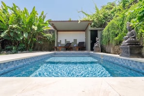 Piscina com espreguiçadeiras, área de estar coberta e uma estátua.