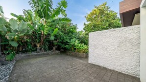 Un patio empedrado con una pared blanca y exuberante vegetación tropical.