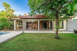 Ein modernes Haus mit Schwimmbad, einem gepflegten Rasen und einem großen Baum im Vorgarten.