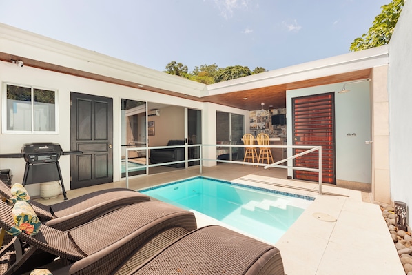 A modern outdoor pool area with wicker lounge chairs, a barbecue grill, and a covered patio.