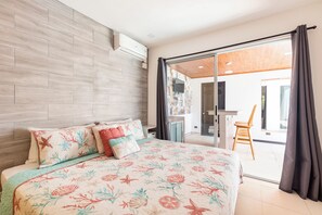 A bedroom with a bed, a wooden headboard, a sliding glass door leading to a balcony, and a small table with a chair.