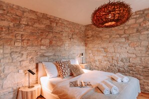 A bedroom with a stone wall, a bed with white bedding, a patterned pillow, a bedside lamp, and a woven light fixture. - Istrian Villa Beatrice near Pula, Galižana, Croatia (Galižana)
