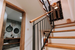 Een trap met houten treden en zwarte leuningen, leidend naar een kamer met een ronde spiegel en een houten deur.