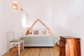 Een slaapkamer met een bed, een stoel, een nachtkastje, een lamp en een houten kast.