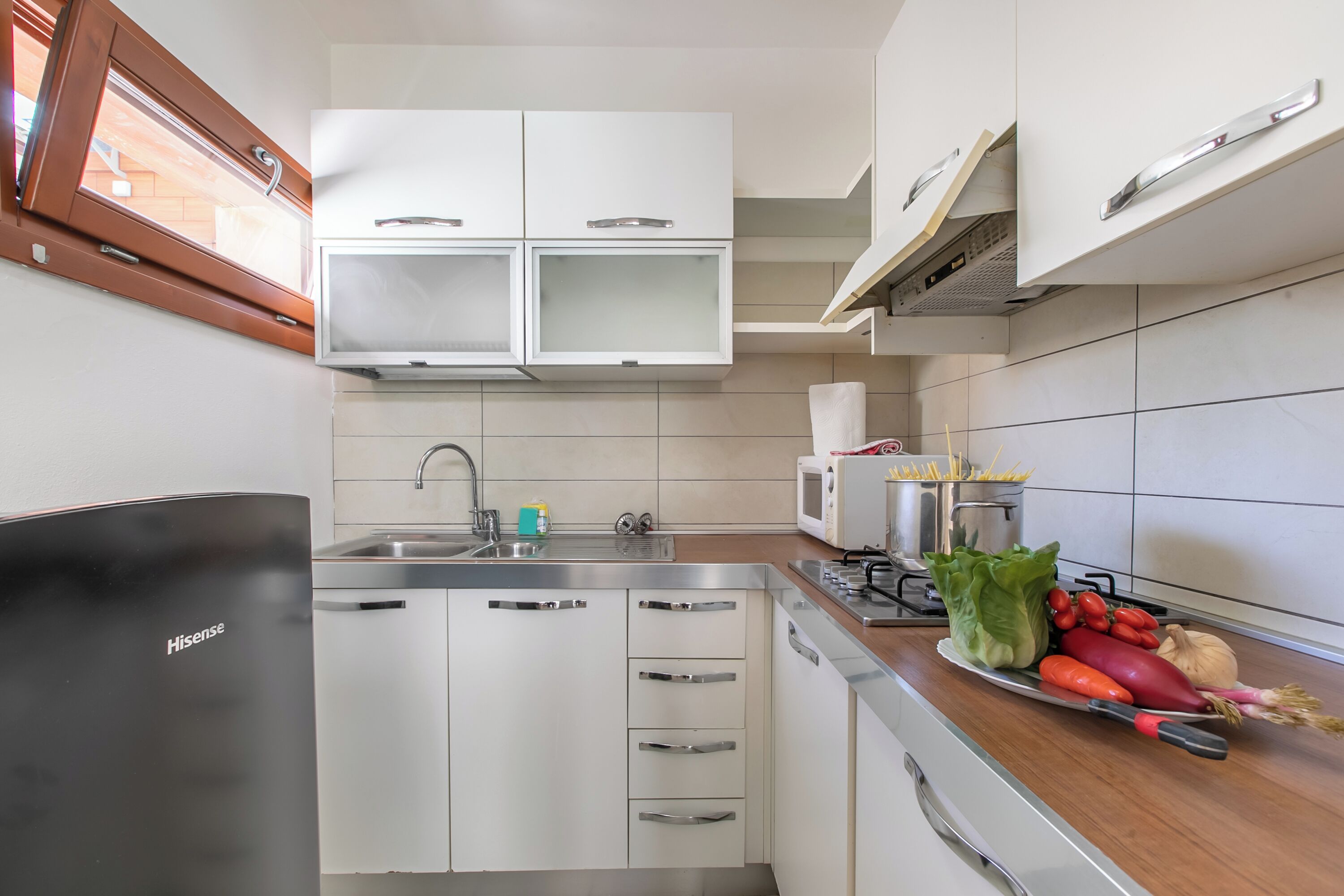A modern kitchen with white cabinets, stainless steel appliances, and a wooden countertop with fresh vegetables.