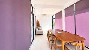A modern interior with a wooden dining table, a sofa, and a sliding glass door leading to a balcony. - Casa De Munggu (Tabanan)