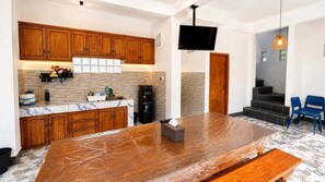 A kitchen with wooden cabinets, a marble countertop, a large wooden table, a black refrigerator, and a TV mounted on the wall. - Casa De Munggu (Tabanan)