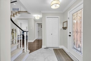 A hallway with a staircase, a white door, and a stained glass window. - Modern 4BR Family Home w/ Pool · Whitby (Whitby)