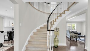 A modern interior with a curved staircase, a dining area, and a living room. - Modern 4BR Family Home w/ Pool · Whitby (Whitby)