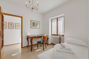 A hotel room with a bed, a desk with a chair, a chandelier, and framed artwork on the walls. - Kirribilli House, Nago-Torbole, Italy (Nago-Torbole)