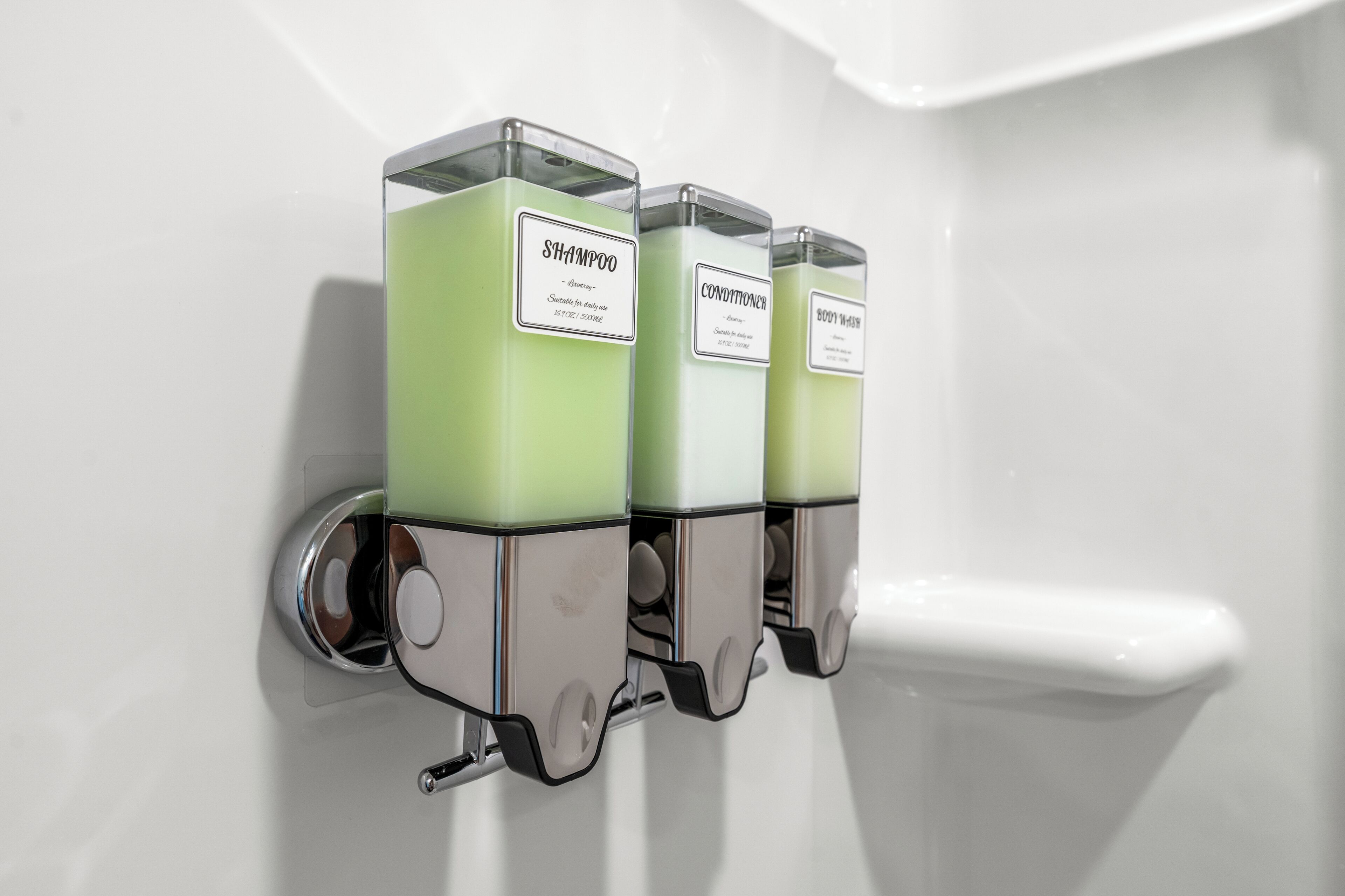 Three dispensers labeled shampoo, conditioner, and body wash mounted on a wall.