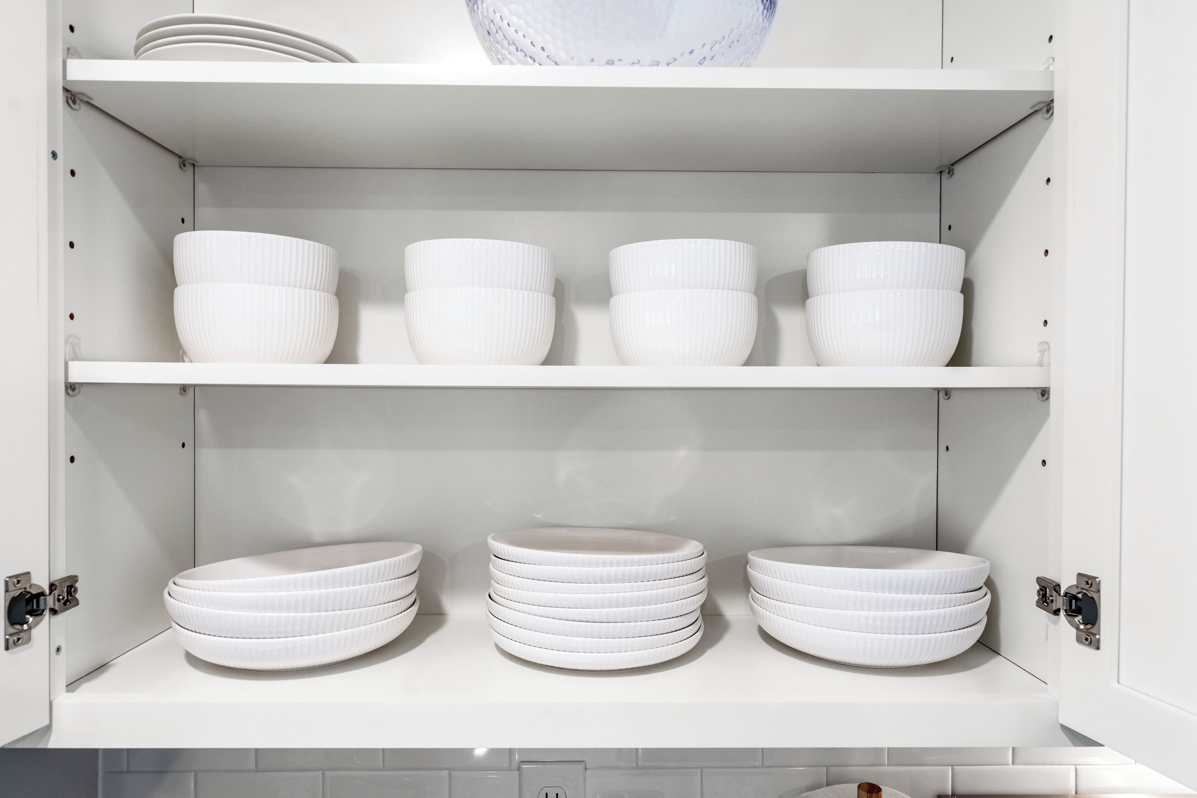 Un meuble blanc avec des étagères où sont rangés des bols et des assiettes blancs.