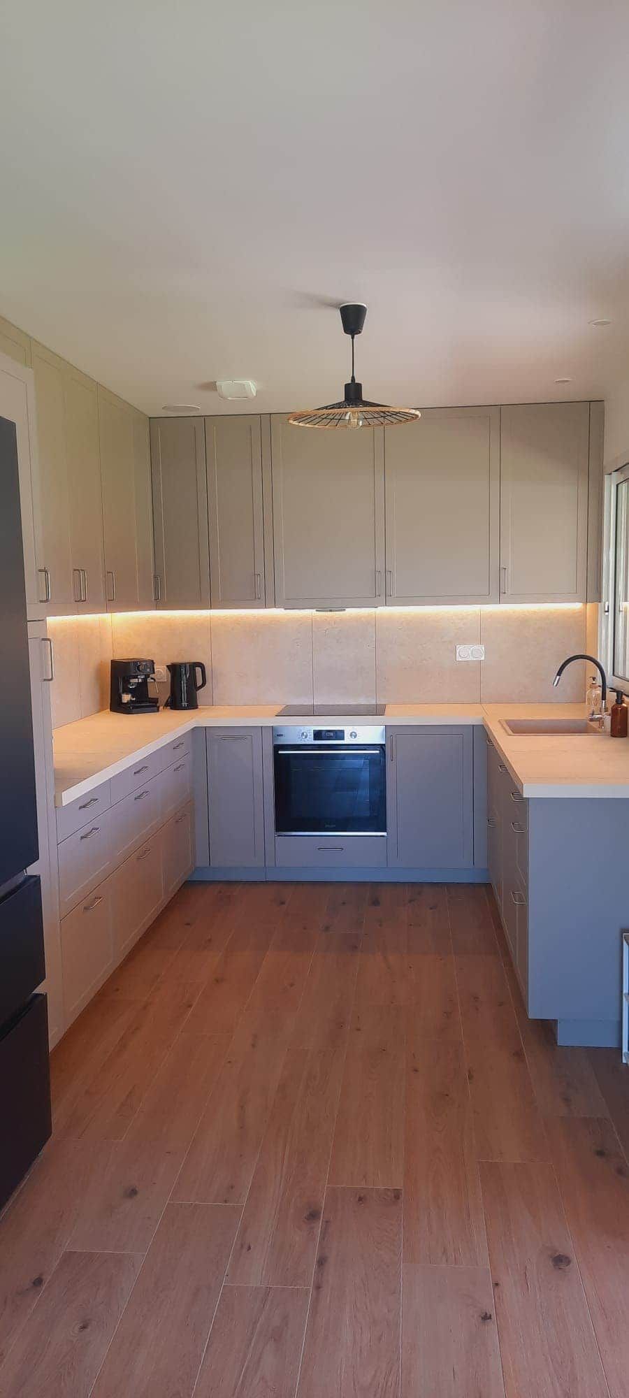 Una cocina moderna con suelo de madera, armarios empotrados, una isla central y una lámpara colgante.