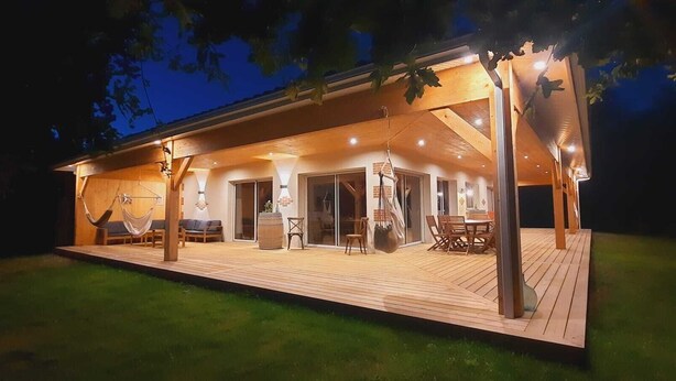 Ein modernes Haus mit einer Holzterrasse, Sitzgelegenheiten und einem Essbereich im Freien.
